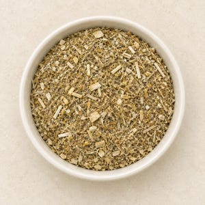Può includere: Una ciotola bianca rotonda riempita con una miscela di erbe secche composta da fibre vegetali finemente tritate di colore beige e marrone chiaro, piccoli frammenti di steli legnosi e particelle botaniche strutturate, creando un aspetto denso e granulare.