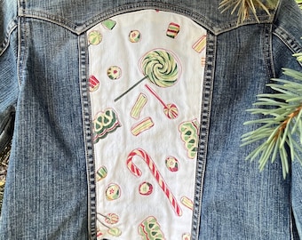 May include: A blue denim jacket with a white patch on the back. The patch features a repeating pattern of candy canes, lollipops, and other sweets.