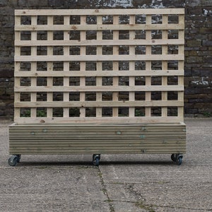 May include: A wooden planter box with a trellis on wheels. The planter is made of natural wood and has a slatted design. The trellis is made of a grid pattern and is attached to the planter. The planter is on four wheels and is ready to be moved around a garden or patio.