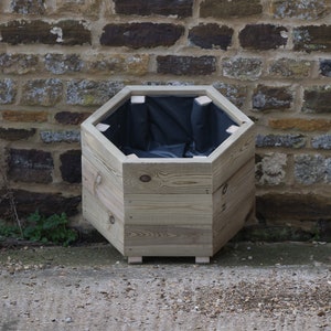 May include: A hexagonal wooden planter with a black liner. The planter is made of natural wood and has a rustic look. It is sitting on a concrete surface.