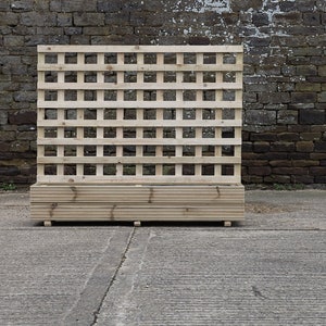May include: A wooden planter with a lattice panel on the back. The planter is made of natural wood and has a rectangular shape. The lattice panel is made of thin wooden slats that are arranged in a grid pattern.