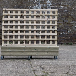 May include: A wooden planter box with a trellis on the back. The planter is on wheels and has a natural wood finish.
