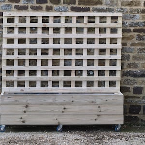 May include: A wooden planter box with a trellis on top. The planter box is on wheels and has a natural wood finish. The trellis is made of thin wooden slats.