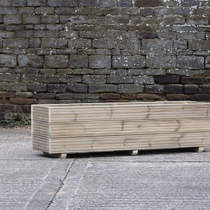 May include: A rectangular wooden planter box with a natural finish. The planter is made of horizontal slats of wood and has a simple design.