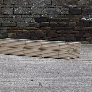 May include: A long, rectangular wooden planter box with a natural wood finish. The planter is made of horizontal slats and has a slightly rounded edge.
