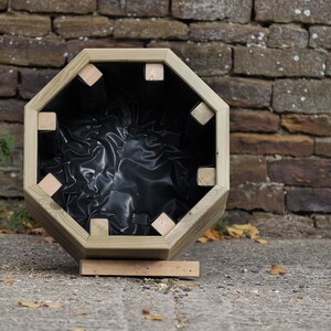 May include: An octagonal wooden planter with a black liner. The planter is empty and sitting on a wooden base.