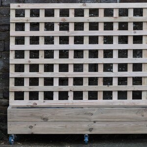 May include: A wooden planter with a trellis on the back. The planter is on wheels and has a natural wood finish.