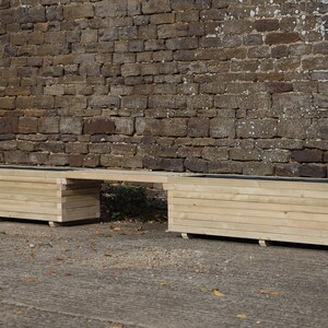 May include: A long wooden planter box with a bench seat in the middle. The planter box is made of natural wood and has a rustic look. The bench seat is also made of wood and has a natural finish.