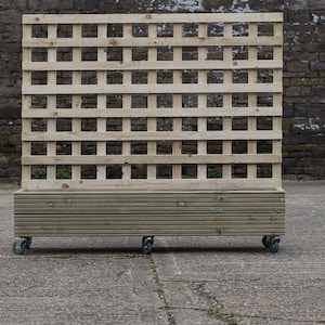 May include: A wooden planter box with a trellis on wheels. The planter is made of natural wood and has a slatted design. The trellis is made of a grid pattern and is attached to the planter. The planter is on four wheels and is ready to be moved around a garden or patio.