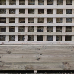 May include: A wooden planter box with a trellis attached to the back. The planter box is made of natural wood and has a rustic look. The trellis is made of thin wooden slats and is designed to support climbing plants.