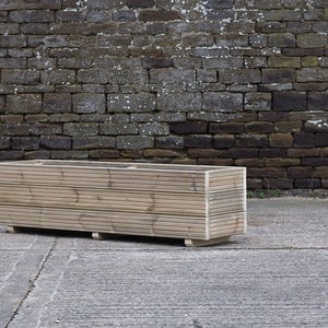 May include: A long, rectangular wooden planter box with a natural finish. The planter is made of horizontal slats of wood and has a simple, modern design.