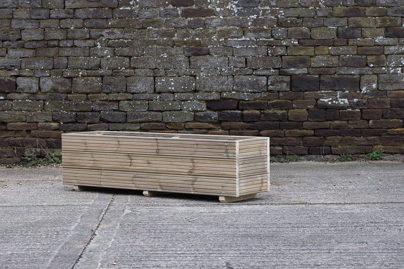 May include: A long, rectangular wooden planter box with a natural finish. The planter is made of horizontal slats of wood and has a simple, modern design.