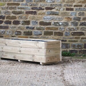May include: A wooden planter box with three horizontal slats. The planter is made of natural wood and has a rustic look.