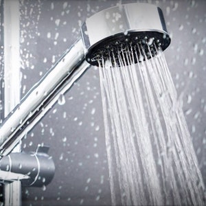 May include: A chrome shower head with a spray of water coming out of it. The shower head is attached to a chrome pipe.