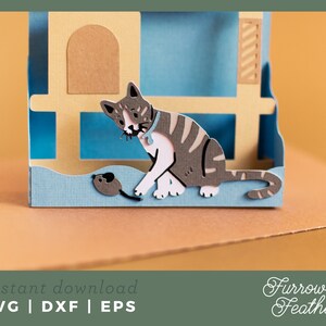 May include: A papercraft cat house with a gray and white cat looking at a small gray mouse. The house is made of brown and blue paper and has a window and a door. The cat is sitting on a blue platform and the mouse is on the ground.