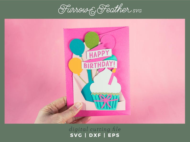 May include: A pink card with a pop-up cupcake design. The cupcake is white with pink frosting and a green and blue wrapper. The card has a banner that says "Happy Birthday!" with balloons in the background.