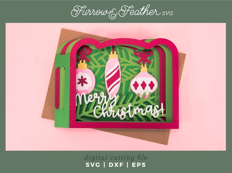 May include: A layered Christmas card with a pink and green design. The card features three hanging ornaments and the words "Merry Christmas". The card is set against a pink background.