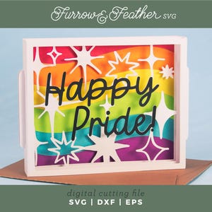 May include: A layered paper craft display in a white frame featuring a rainbow background with white star cutouts and the black text Happy Pride! in a script font. The design includes wavy horizontal stripes of red, orange, yellow, green, blue, and purple.