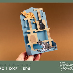 May include: A blue and brown cat tree with three levels, a cat toy, and three cats. The top level has a brown cat, the middle level has a black cat, and the bottom level has a gray and white cat. The cat tree is made of paper and is a digital download.