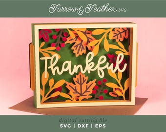 Pode incluir: Uma peça de arte em papel em camadas com a palavra "thankful" em escrita branca. O design apresenta folhas de outono em tons de laranja, amarelo e vermelho, com um fundo verde. O texto "Furrow & Feather SVG" está no topo.