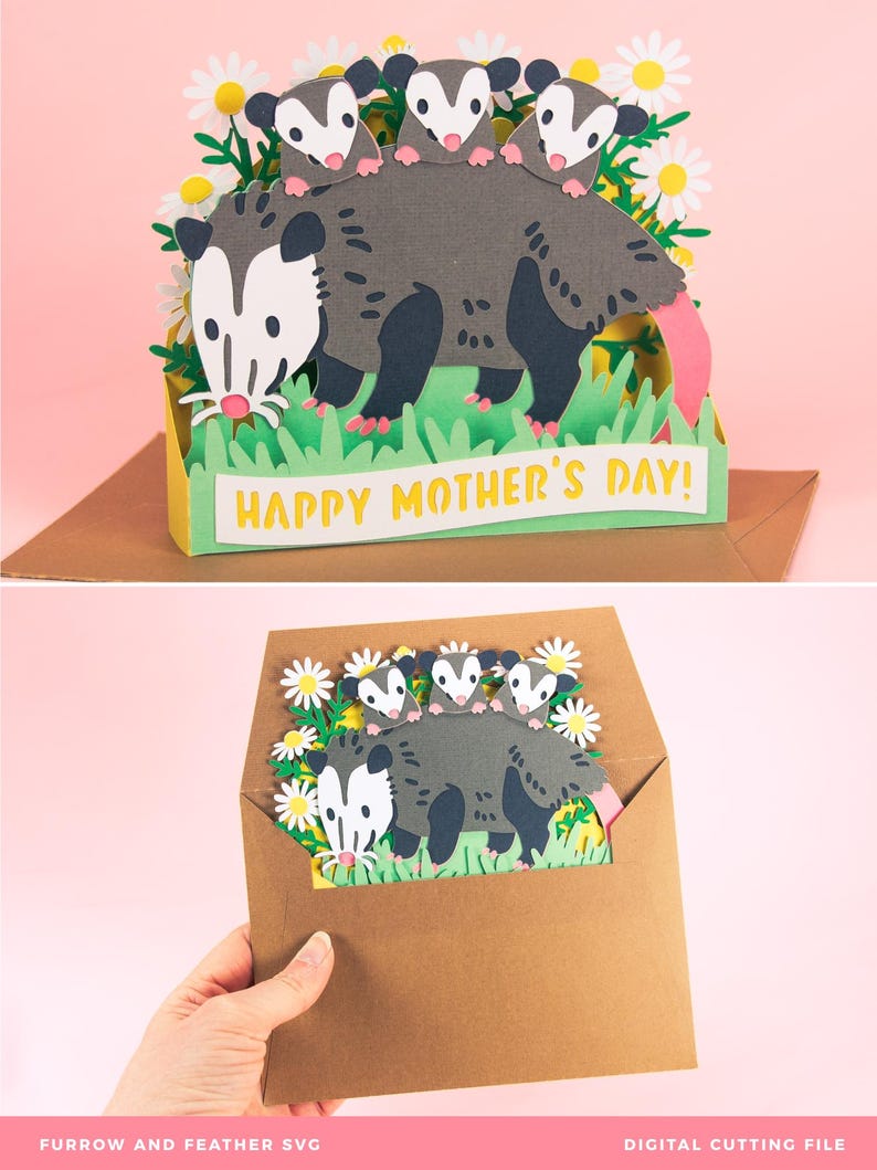 May include: A papercraft Mother's Day card depicting a grey opossum with three babies, white daisies, and green grass. The card reads "Happy Mother's Day!" in yellow. The card is presented inside a brown envelope, perfect for gifting.