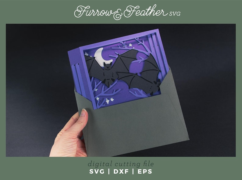 Pode incluir: Uma pe&ccedil;a de arte em papel em camadas com tema de Halloween. O design inclui morcegos pretos, uma lua crescente branca e &aacute;rvores estilizadas em um fundo roxo. A obra de arte &eacute; mantida em um envelope cinza. O texto na imagem diz "Furrow & Feather SVG" e "digital cutting file".
