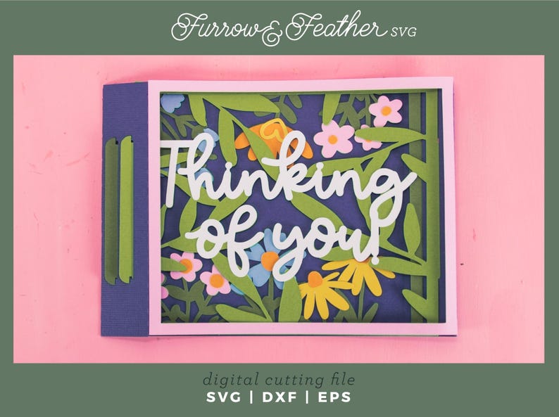 May include: A paper card with the words "Thinking of you" in white script, featuring a floral design with green leaves and colourful flowers. The background is a deep blue, set against a pink backdrop. The card is a digital cutting file.