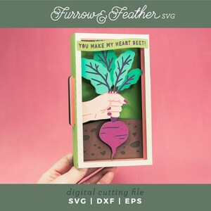 May include: A digital cutting file for a card with a beet and the text "YOU MAKE MY HEART BEET!" The beet is green and purple and is being held by a hand. The card is in a frame with a green and white border.
