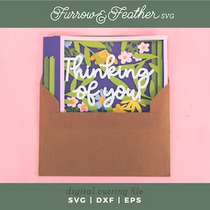 May include: A paper card with the words "Thinking of you" in white script, surrounded by a floral design, is partially inserted into a brown envelope. The card is set against a purple background with green leaves and colorful flowers. The image includes the text "Furrow & Feather SVG" and "digital cutting file SVG | DXF | EPS".