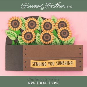 May include: A papercraft of sunflowers in a brown wooden crate with green leaves. The sunflowers have yellow petals and brown centres. The crate has the text "SENDING YOU SUNSHINE!" on a yellow banner. The image has the text "Furrow & Feather SVG".