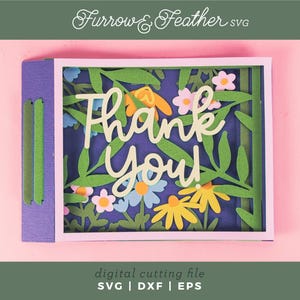 May include: A layered paper art card with the words "Thank You" in a cursive font, surrounded by floral cutouts. The card features a purple base with green and blue accents, set against a pink background.