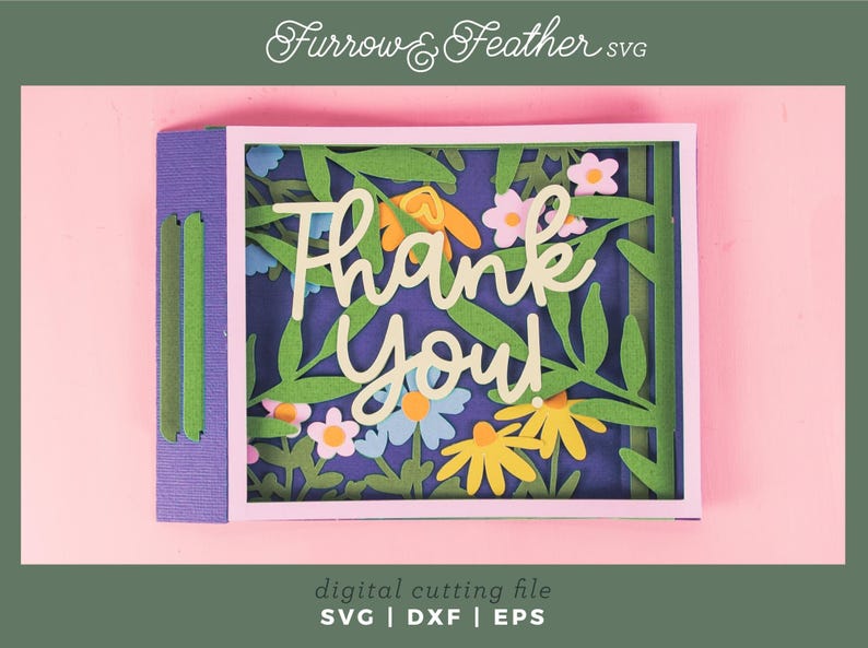 May include: A layered paper art card with the words "Thank You" in a cursive font, surrounded by floral cutouts. The card features a purple base with green and blue accents, set against a pink background.