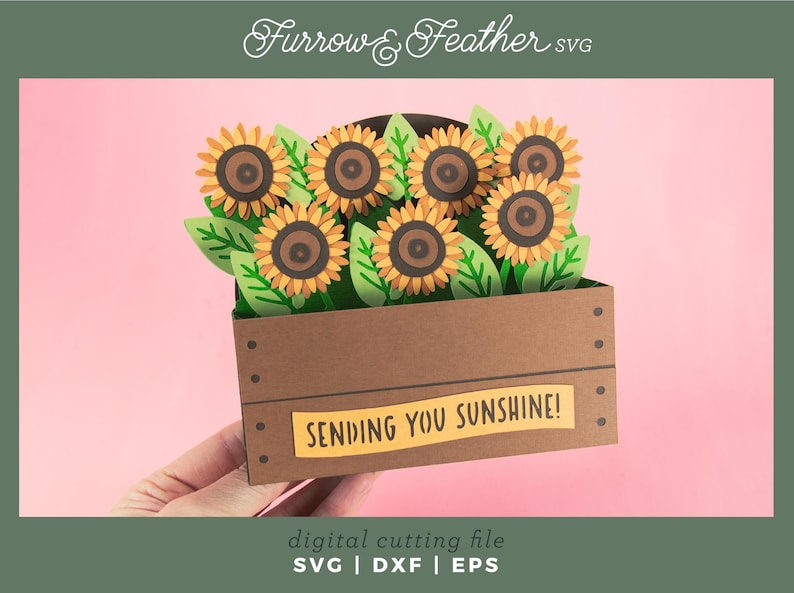 May include: A papercraft of sunflowers in a brown wooden crate with the text "SENDING YOU SUNSHINE!". The sunflowers have yellow petals and brown centres, with green leaves. The image is a digital cutting file.