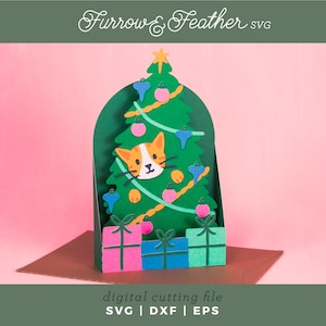 May include: A green Christmas tree card featuring a cat face, baubles, and presents. The card has the text "Furrow & Feather SVG" and "digital cutting file SVG | DXF | EPS". The background is pink.