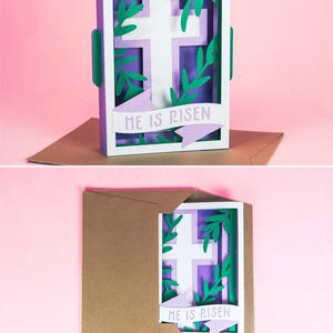 May include: A purple and white papercraft card with a white cross surrounded by green leaves. The card is open to reveal a purple banner with the text "He is Risen".