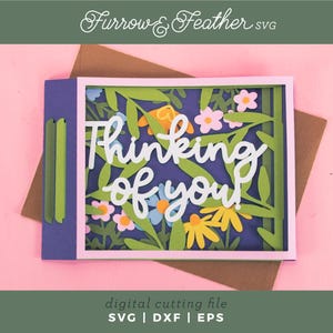 May include: A paper card with the words "Thinking of You" in white script, surrounded by colourful flowers and leaves. The card is set against a pink background, with the text "digital cutting file" and file type abbreviations at the bottom.