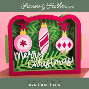 May include: A layered Christmas card design with a red and green frame, featuring three pink ornaments with white accents against a green fir tree background. The words "Merry Christmas!" are in white script. The design is labeled as a digital cutting file.