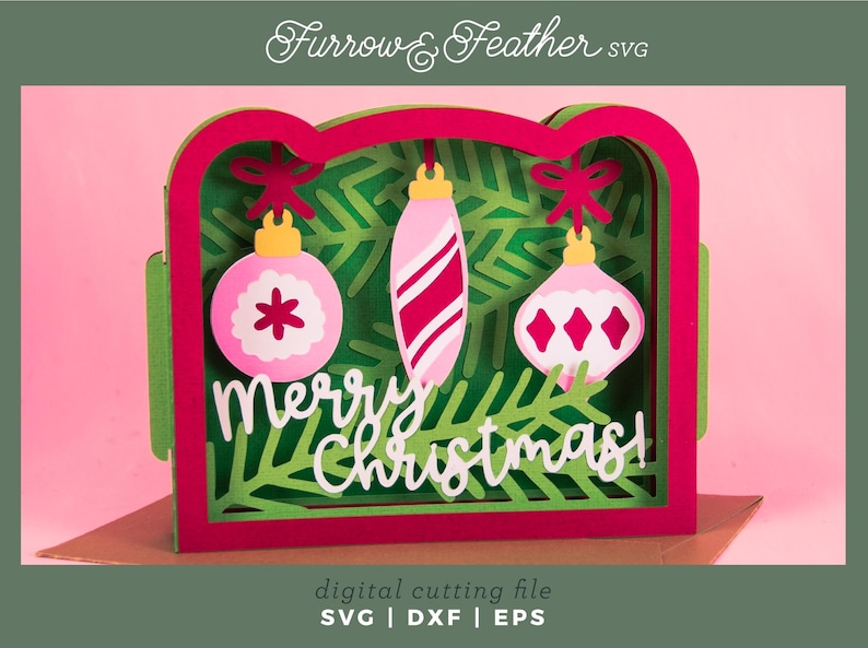 May include: A layered Christmas card design with a red and green frame, featuring three pink ornaments with white accents against a green fir tree background. The words "Merry Christmas!" are in white script. The design is labeled as a digital cutting file.