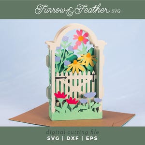 May include: A 3D paper craft structure featuring an arched gate design with a white picket fence, yellow and pink flowers, and green foliage. The text Furrow & Feather SVG and digital cutting file SVG | DXF | EPS is visible on the image.