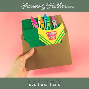 May include: A brown envelope with a green card inside. The card has a yellow and green design with the words "Thank You!" in pink letters. There are six colorful crayons sticking out of the top of the card.