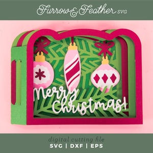 May include: A layered Christmas-themed papercraft design with pink, green, and red accents. The design features three hanging ornaments and the words "Merry Christmas!" in white. The image is a digital cutting file.