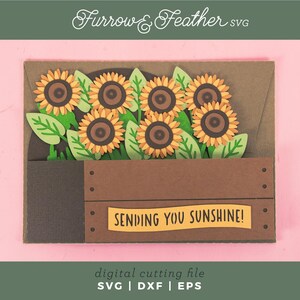 May include: A papercraft greeting card with sunflowers in a wooden crate. The sunflowers have yellow petals and brown centres, with green leaves. The card includes the text "SENDING YOU SUNSHINE!" and "Furrow & Feather SVG".