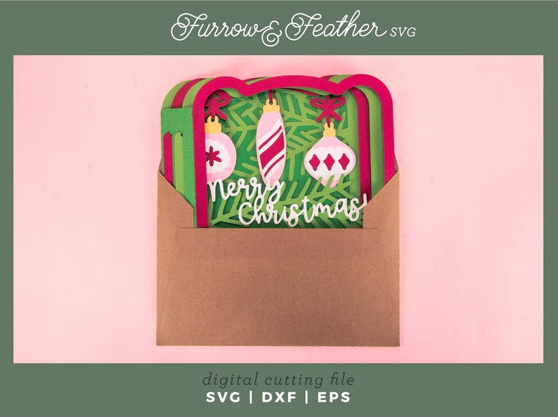 May include: A layered paper Christmas card design in a brown envelope. The card features green and red layers with three hanging ornaments and the words "Merry Christmas". The design is set against a pink background. The text "Furrow & Feather SVG" is at the top.