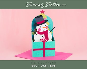 May include: A digital cutting file for a snowman popping out of a turquoise gift box with a red ribbon. The snowman is wearing a black top hat and a red scarf. The file is available in SVG, DXF, and EPS formats.