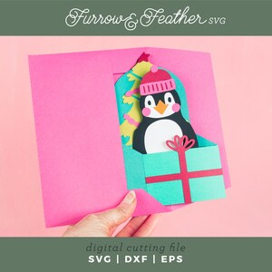 May include: A pink card with a pop-up penguin wearing a red and white hat. The penguin is holding a green and red gift box. The card says "Furrow & Feather svg" at the top and "digital cutting file SVG | DXF | EPS" at the bottom.