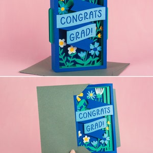 Może przedstawiać: Błękitna i zielona kartka z papieru z wyskakującym elementem. Kartka przedstawia wz&oacute;r kwiatowy z banerem z napisem "Congrats Grad!"