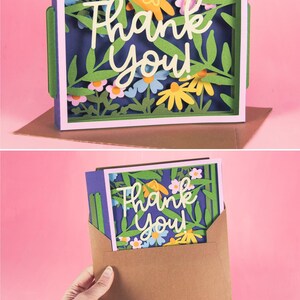 May include: A layered paper art card with a floral design and the words "Thank You" in white script. The card features green leaves, and colorful flowers in a white frame. The card is inside a brown envelope.