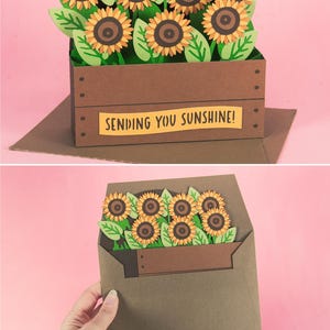 May include: A brown paper card featuring a 3D sunflower arrangement. The sunflowers have yellow petals and brown centres, with green leaves. The card reads "SENDING YOU SUNSHINE!"