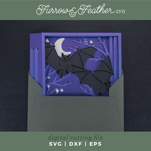 Pode incluir: Uma pe&ccedil;a de arte em papel em camadas com tema de Halloween. O design inclui morcegos pretos, uma lua crescente branca e estrelas em um fundo roxo. A obra de arte &eacute; apresentada em um envelope cinza escuro. O texto na imagem diz "Furrow & Feather SVG" e "digital cutting file SVG | DXF | EPS".