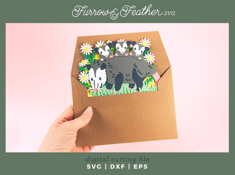 May include: A brown paper envelope contains a paper cut-out scene of a possum family amongst daisies. The possum is grey with a white face and pink tail. The text "Furrow & Feather SVG" is at the top.